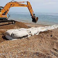 Instalação de sacos SoilTain numa praia de cascalho com draga para proteção contra inundações