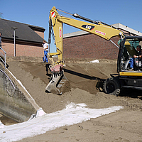 Escavadora espalha solo sobre tapetes de bentonite Tektoseal® Clay para estabilizar um pequeno declive