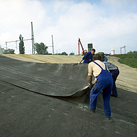 Trabalhadores no processo de colocação do tapete de bentonite HUESKER num estaleiro de impermeabilização.